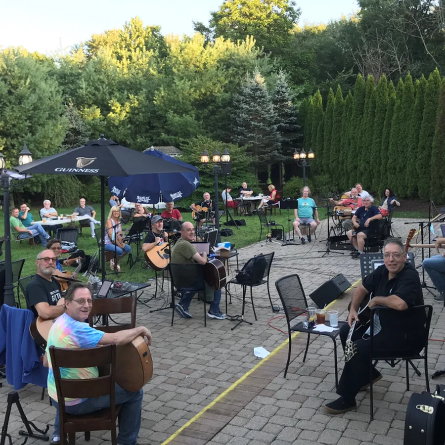 Musicians with guitars playing together around tables on an outdoor patio at an evening jam.