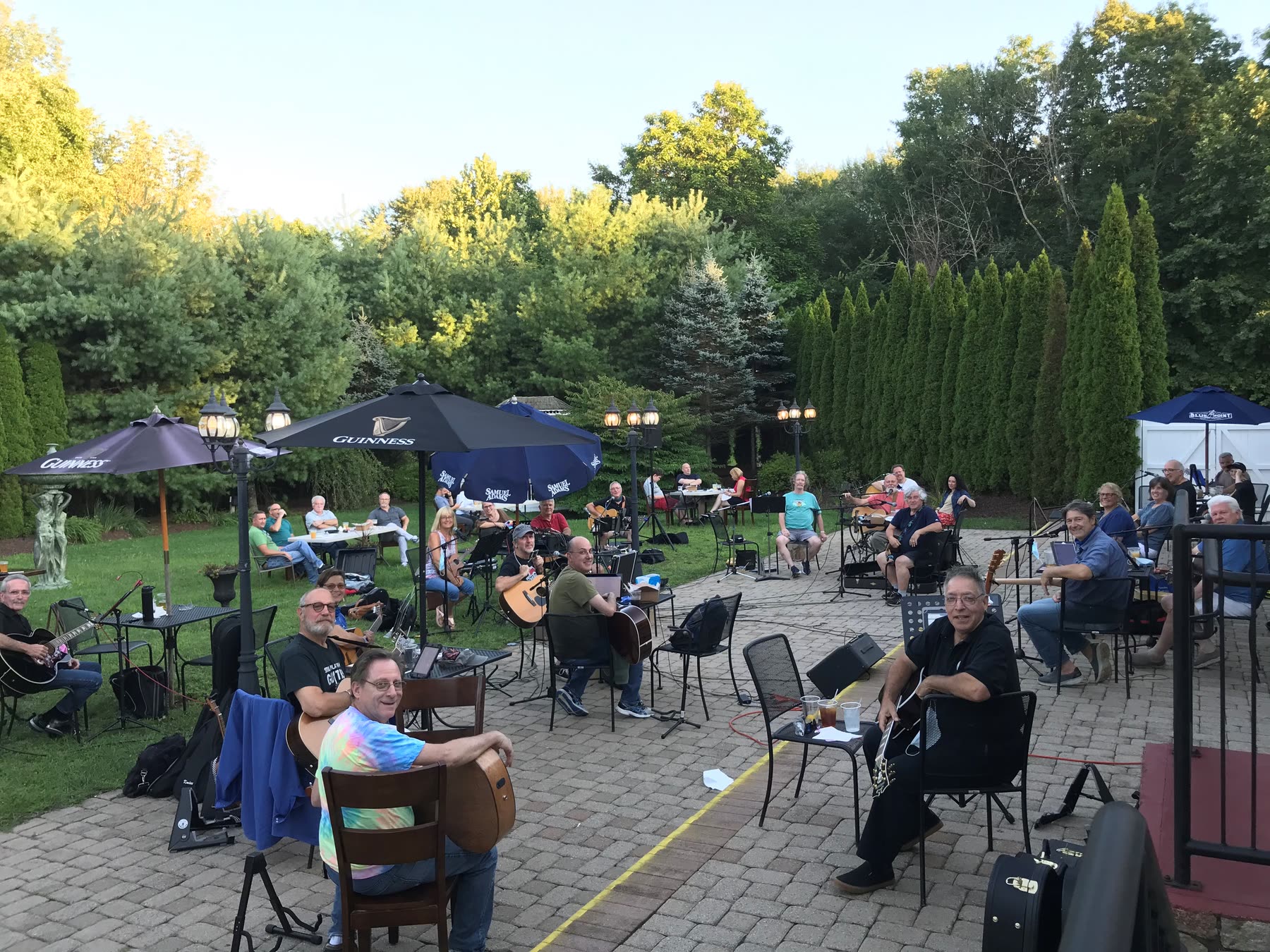 An evening jam on a garden patio, musicians seated under umbrellas with guitars.