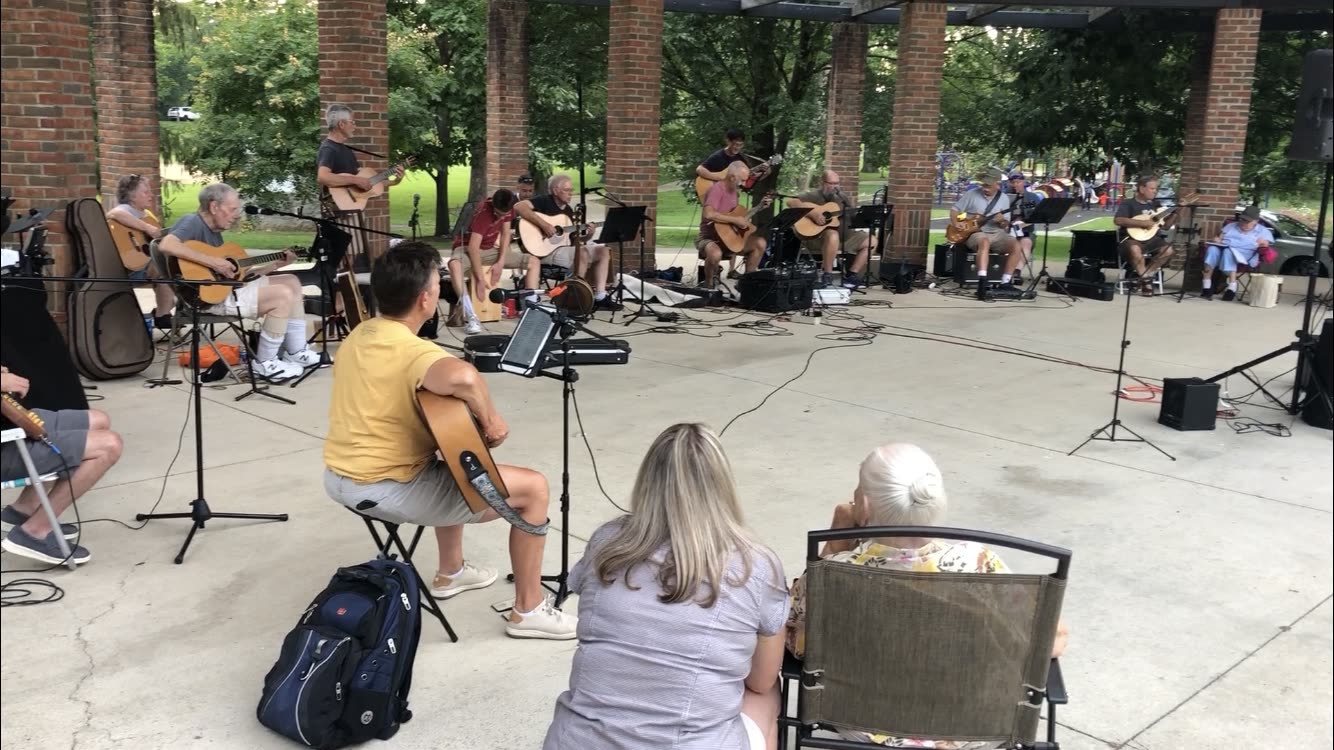 Musicians and listeners gathered in a circle at an outdoor pavilion jam.